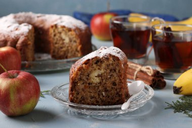 Elma, muz ve tarçınlı ev yapımı kek, açık mavi arkaplanda şekerle serpiştirilmiş. Parça ön planda.