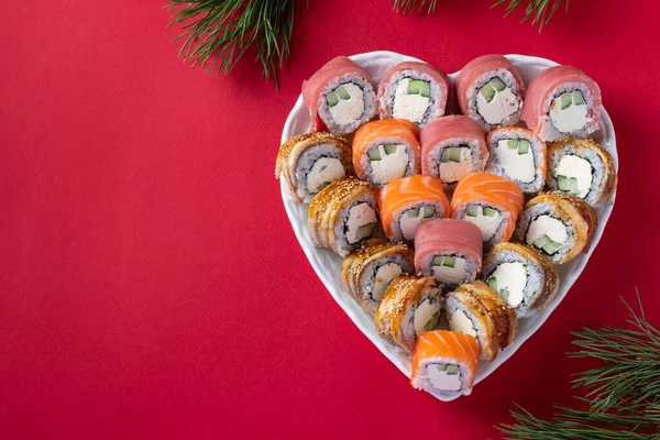 Jedzenie azjatyckie z zestawem sushi z łososia, tuńczyka i węgorza z serem filadelfijskim na talerzu w kształcie serca na czerwonym tle. Widok góry. Miejsce na tekst — Zdjęcie stockowe