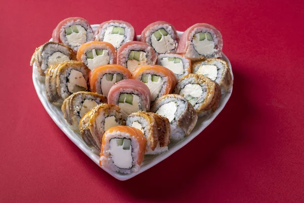 Zestaw sushi z łososia, tuńczyka i węgorza z serem filadelfijskim w talerzu jako serce na czerwonym tle. Walentynki żywności koncepcja. — Zdjęcie stockowe