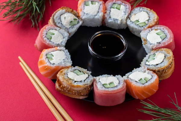 Świąteczne brunch sushi zestaw łososia, tuńczyka i węgorza z serem Philadelphia jako wieniec na czerwonym tle. Zbliżenie — Zdjęcie stockowe