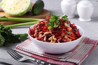 Taze sebzelerden salata: lahana, pancar, havuç, salatalık, soğan ve gri arka planda beyaz kasede maydanoz.