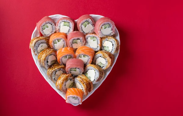 Sushi set of salmon, tuna and eel with philadelphia cheese in plate as heart on red background. Valentine day food concept. Top view. Space for text