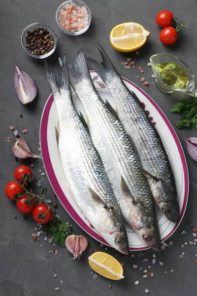 Fresco listo para cocinar salmonetes crudos con ingredientes y condimentos como perejil, limón, tomates cherry, cebolla roja y aceite de oliva sobre fondo oscuro. Vista superior — Foto de Stock