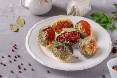 Değişik baharat ve mısır gevreğiyle süslenmiş paskalya yumurtaları boyasız ve gri beton arka planda beyaz bir tabakta koruyucuları var..