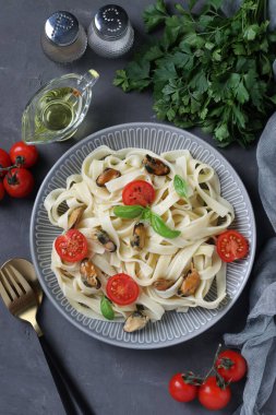 Tagliatelle makarnası, midye ve kiraz domatesli gri tabakta. Dikey. Flatlay biçimi.