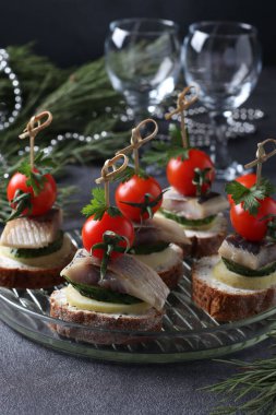 Tuzlu ringa balığı, salatalık, haşlanmış patates, vişneli domates ve gri arka planda çavdar ekmeği üzerine siyah zeytin. Dikey biçim