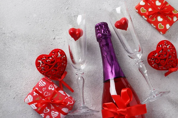 Sticla de sampanie roz, doua pahare cu inimi de bomboane si cadouri pe fundal gri. Conceptul de Valentine Day. Vedere de sus . — Fotografie, imagine de stoc