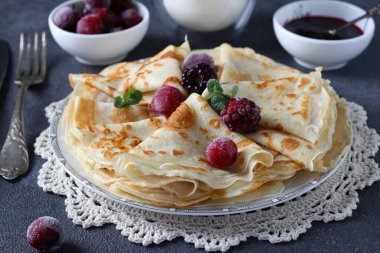 İnce krep, buğday unu, yumurta ve kefir, böğürtlen, reçel ve gri masada bir bardak süt ile servis edilir.