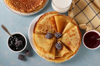 Mısır unundan yapılan ev yapımı ince krepler, böğürtlen, reçel ve açık mavi arka planda bir fincan sütle servis ediliyor. Yakın plan. Üst görünüm