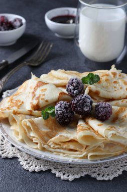 Buğday unu, yumurta ve kefir ile ince krepler, böğürtlen, reçel ve koyu gri masada bir bardak süt ile servis edilir.
