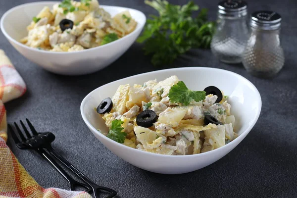 İki tabak salata ananaslı, fırında tavuk, omlet ve siyah zeytinli siyah arka planda beyaz kaseler.