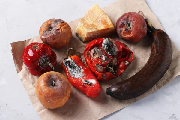 Spoiled rotten foods with mold: apples, peppers, hard cheese and banan on gray background