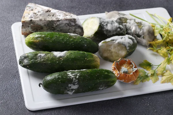 Spoiled rotten foods with mold: cucumbers, hard cheese, parsley and half a lemon on gray background