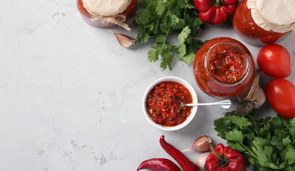 Ermeni kırmızı biber, domates, sarımsak, kişniş ve maydanozdan oluşan bir kap ve gri arka planda kavanozlar. Üst Manzara. Metin için boşluk
