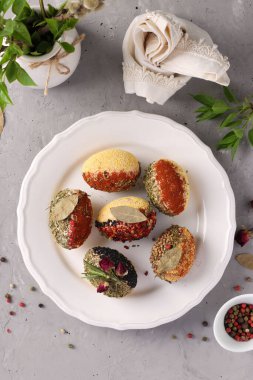 Değişik baharat ve mısır gevreğiyle süslenmiş paskalya yumurtaları gri beton arka planda bir tabakta boya ve koruyucu maddeler olmadan. Üst Manzara. Dikey biçim