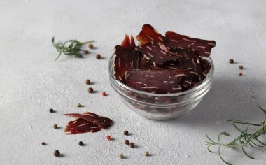 Açık gri arka planda kurutulmuş et, biber ve biberiye. Yatay biçim