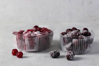Two containers with frozen blackberries and cherries on the light gray background. Harvesting berries for the winter. clipart