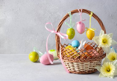 Paskalya tavşanlı sepet ve gri arka planda nergisli renkli yumurtalar. Metin için plase içeren bayram kartı