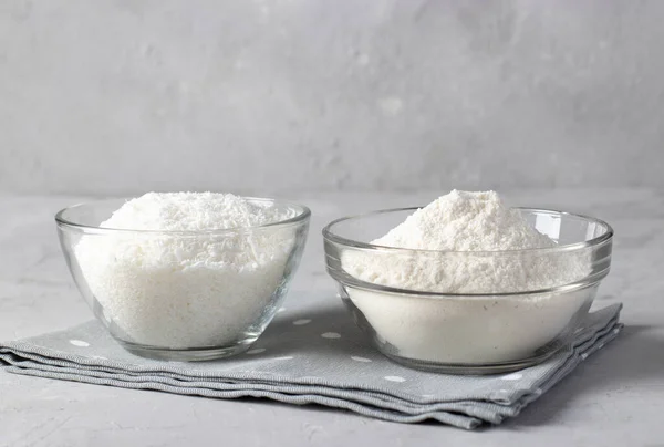 Vegane Kokosnussprodukte: Kokosflocken und Mehl in transparenten Schalen vor grauem Hintergrund. — Stockfoto