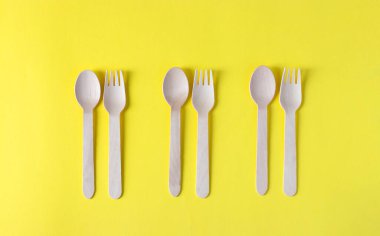 Tahta çatallar ve kaşıklar, sarı arka planda çevre dostu tek kullanımlık mutfak gereçleri. Sıfır atık. Üst görünüm.