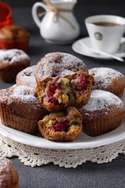 Koyu arkaplanda beyaz bir tabakta üzerine pudra şekeri serpiştirilmiş kirazlı kekler. Dikey biçim