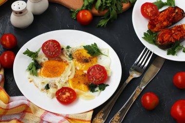 Çırpılmış yumurta ve kiraz domatesleri koyu arkaplanda beyaz bir tabakta, fırında patlıcan ve maydanozlu fotoğraf var.