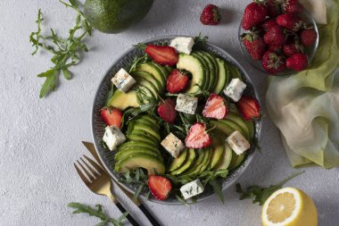 Sağlıklı salata, çilek, avokado, roka ve peynirli lacivert, gri arka planda balzamik bir tabakta. Yukarıdan görüntüle