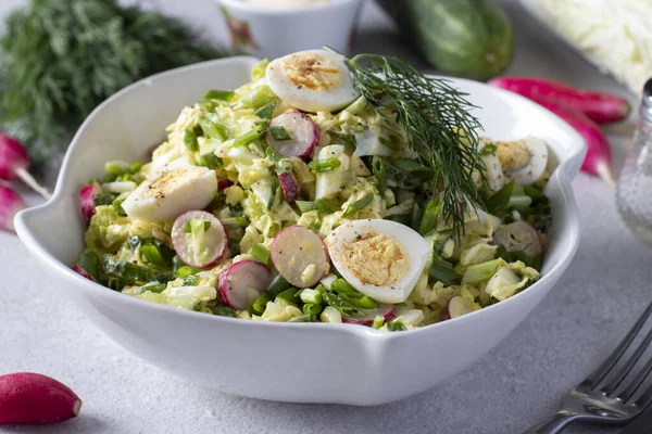 Salată cu varză chinezească, castravete, ridiche, ceapă verde și ouă de prepeliță într-o farfurie albă pe un fundal gri . — Fotografie, imagine de stoc