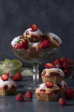 Ev yapımı çilekli kekler üzerine pudra şekeri serpiştirilmiş. Koyu gri bir arka planda hayat.