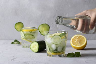 Nane, limon ve salatalıklı iki yaz taze buzlu içecek açık gri arka planda sağlıklı detoks mojito kokteyli. Maden suyu şişeden bardaklara dökülür..