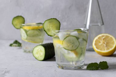 İki yaz boyunca naneli, limonlu ve salatalıklı buzlu içecek artı bir şişe maden suyu. Açık gri arka planda sağlıklı mojito detoks kokteyli.
