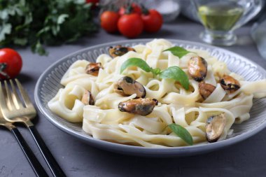Tagliatelle makarnası, gri arka planda bir tabakta midye ve fesleğen. Yakın plan.