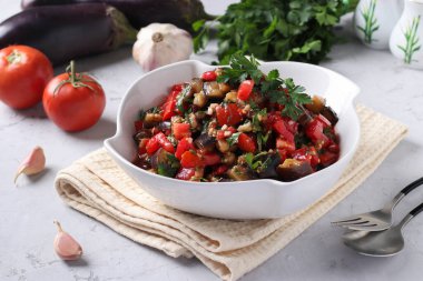 Patlıcanlı salata, domates, sarımsak ve maydanoz açık gri arka planda beyaz bir kasede..