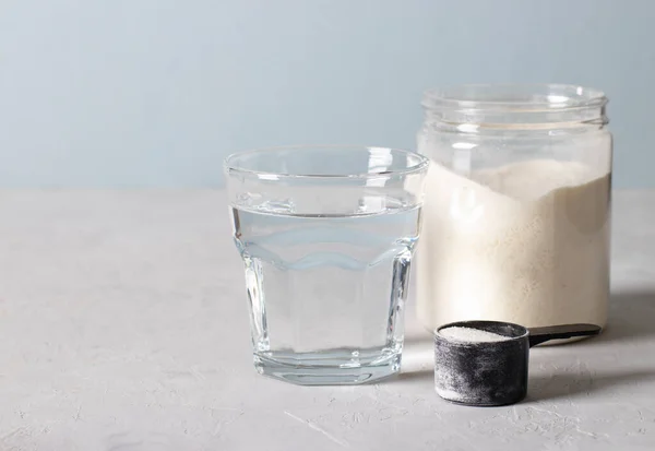 Sticlă de apă, pulbere de colagen în borcan și o lingură de măsurare cu pulbere pe un fundal albastru deschis cu loc pentru text — Fotografie, imagine de stoc