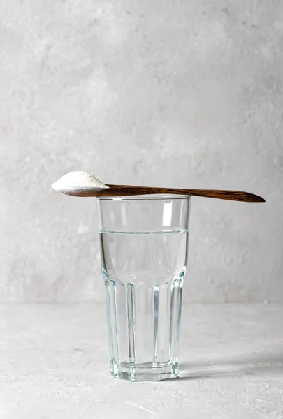 Collagen powder in spoon on glass of water on gray background. Healthy and antiage concept. Vertical format — стоковое фото