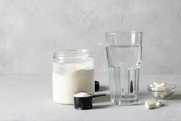 胶原粉装在罐子里，测量勺子、胶原蛋白胶囊和浅灰背景下的一杯水。健康和老年概念 — 图库照片