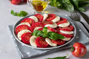 Dilimlenmiş domatesli İtalyan caprese salatası, mozzarella peyniri, fesleğen ve açık gri arka planda zeytinyağı..