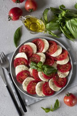 Dilimlenmiş domatesli İtalyan caprese salatası, mozzarella peyniri, fesleğen ve açık gri arka planda zeytinyağı. Yukarıdan görüntüle