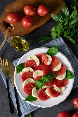 Dilimlenmiş domatesli İtalyan caprese salatası, mozzarella peyniri, fesleğen ve koyu gri arka planda zeytinyağı. Üst görünüm