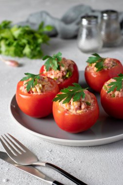 Açık gri arka planda gri bir tabakta jambon ve peynirle doldurulmuş domatesler. Dikey biçim