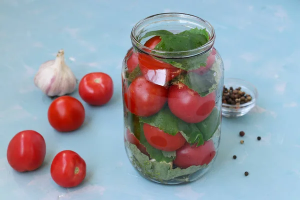 El proceso de preparación de tomates en escabeche con hojas de uva y ajo. Ubicación sobre un fondo azul claro —  Fotos de Stock