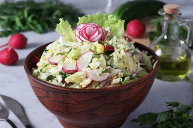 Lahanalı salata, salatalık, turp, maydanoz ve yumurta açık gri arka planda kahverengi bir kasede.