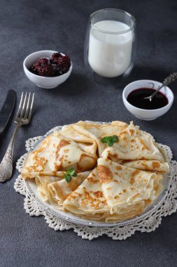Buğday unundan yapılan ince krepler, koyu gri arka planda yumurta ve süt. Dikey biçim