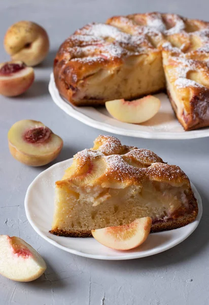 Sliced peach pie sprinkled with powdered sugar on light gray table. Vertical format