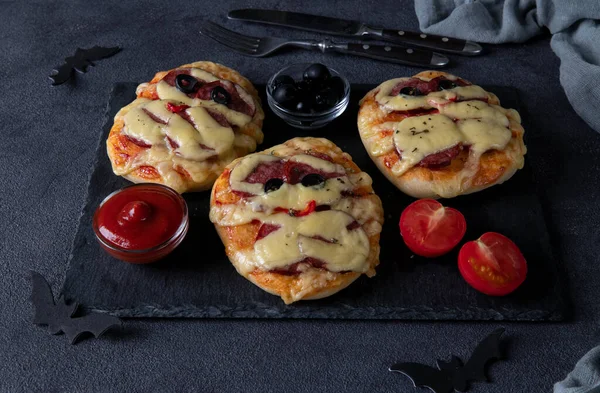 Amuzante mini pizza mumii cu cârnați și brânză pentru petrecerea de Halloween, servite cu măsline negre, ketchup și roșii pe bord întunecat — Fotografie, imagine de stoc