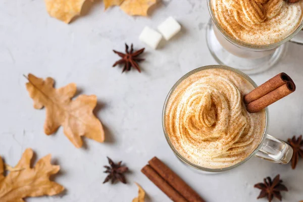 Zwei Glasbecher Kürbislatte mit Gewürzen auf grauem Hintergrund mit Herbstblättern. Blick von oben. — Stockfoto