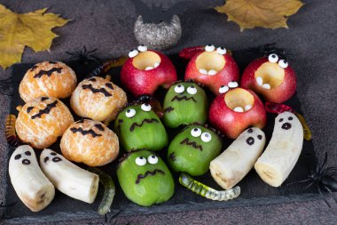 Ürkütücü muz hayaletleri, mandalina, elma ve yeşil kivi canavarları Cadılar Bayramı partisi için tahtada.