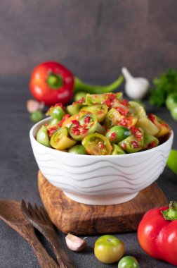 Acı biberli yeşil domates salatası ve tahta tahtadaki beyaz salata kasesinde sarımsak.