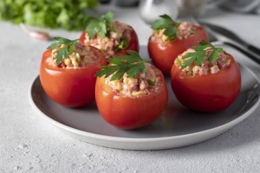 Açık gri arka planda gri tabakta jambon ve peynirle doldurulmuş domatesler.