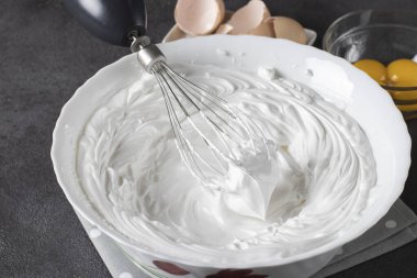 Gri arka planda beyaz kasede çırpılmış krema. Pasta ve kekleri süslemek için krema kullanılır.
